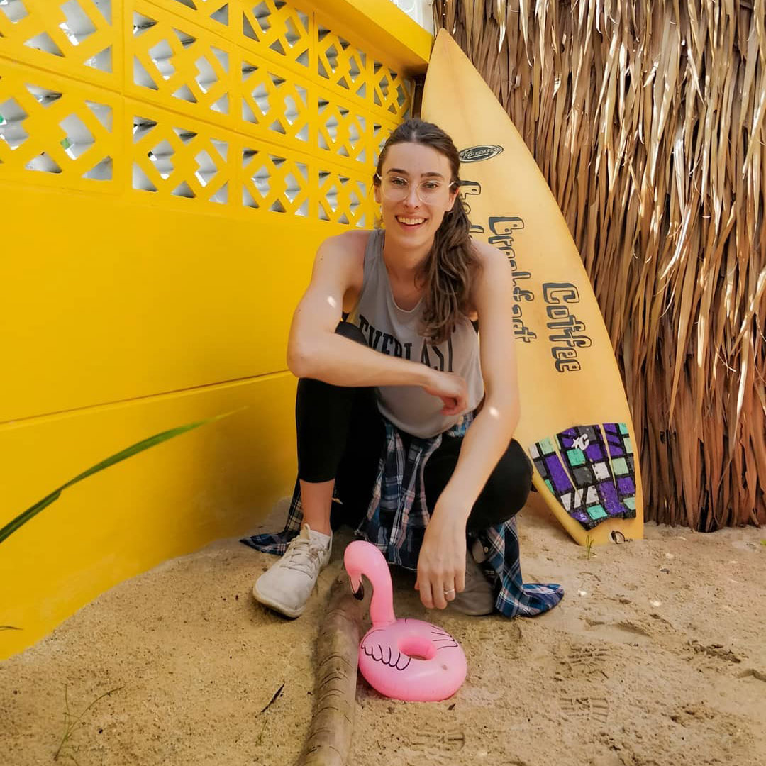 Riley J. Dennis crouching next to an inflatable flamingo with a surfboard behind her.